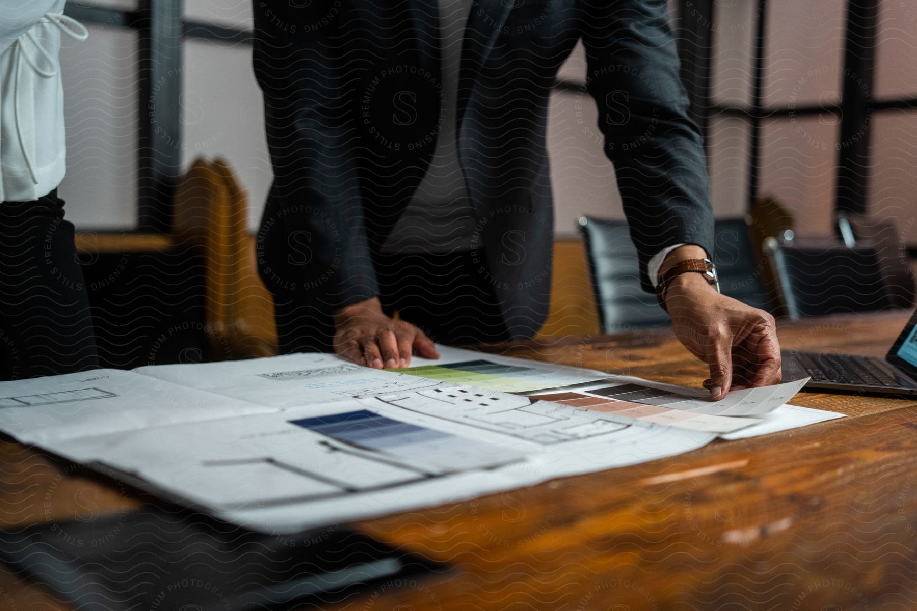 person wearing dark suit stands over presentation papers on conference table