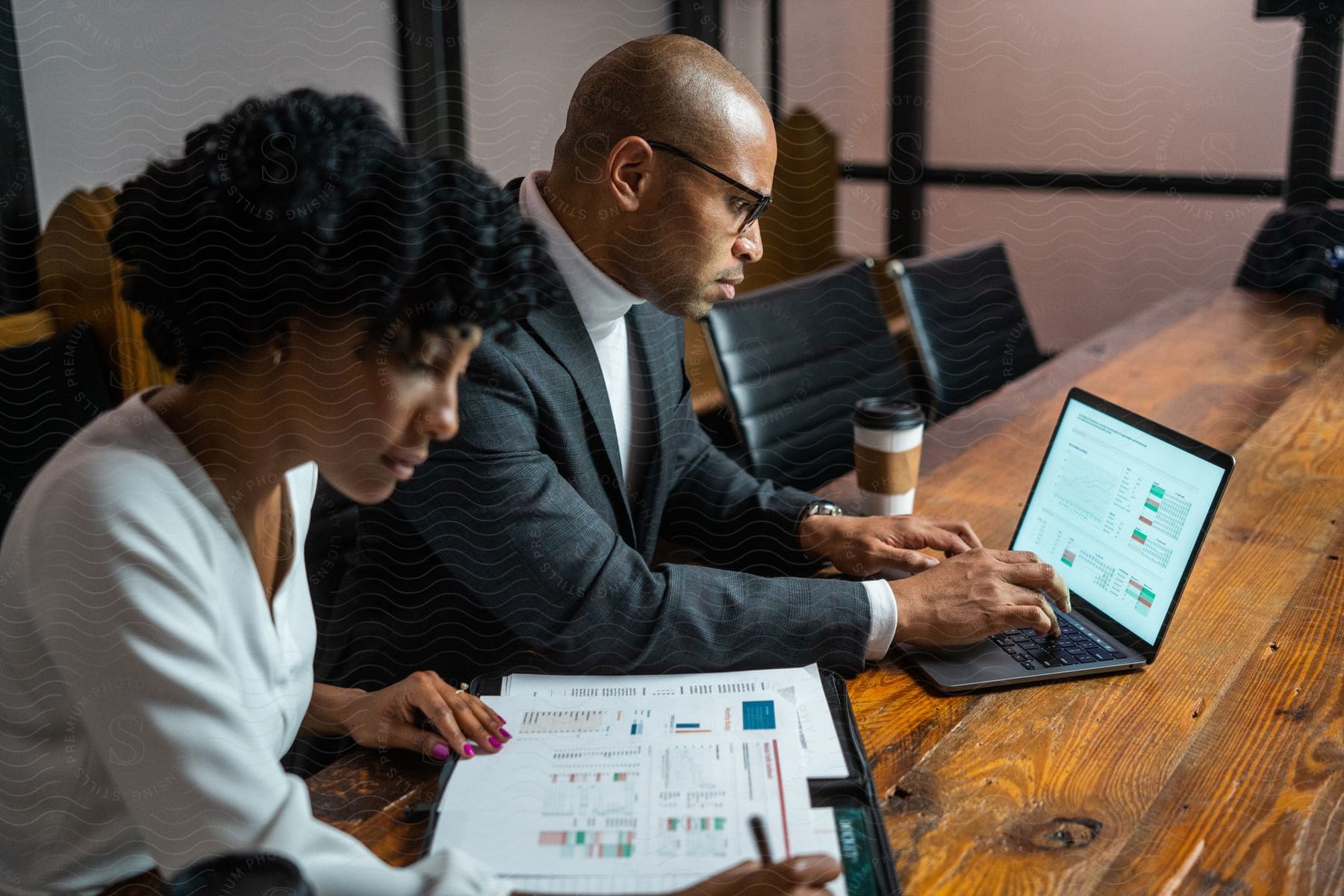 In the office, a businessman diligently works on his laptop while a businesswoman focuses on crafting business reports.