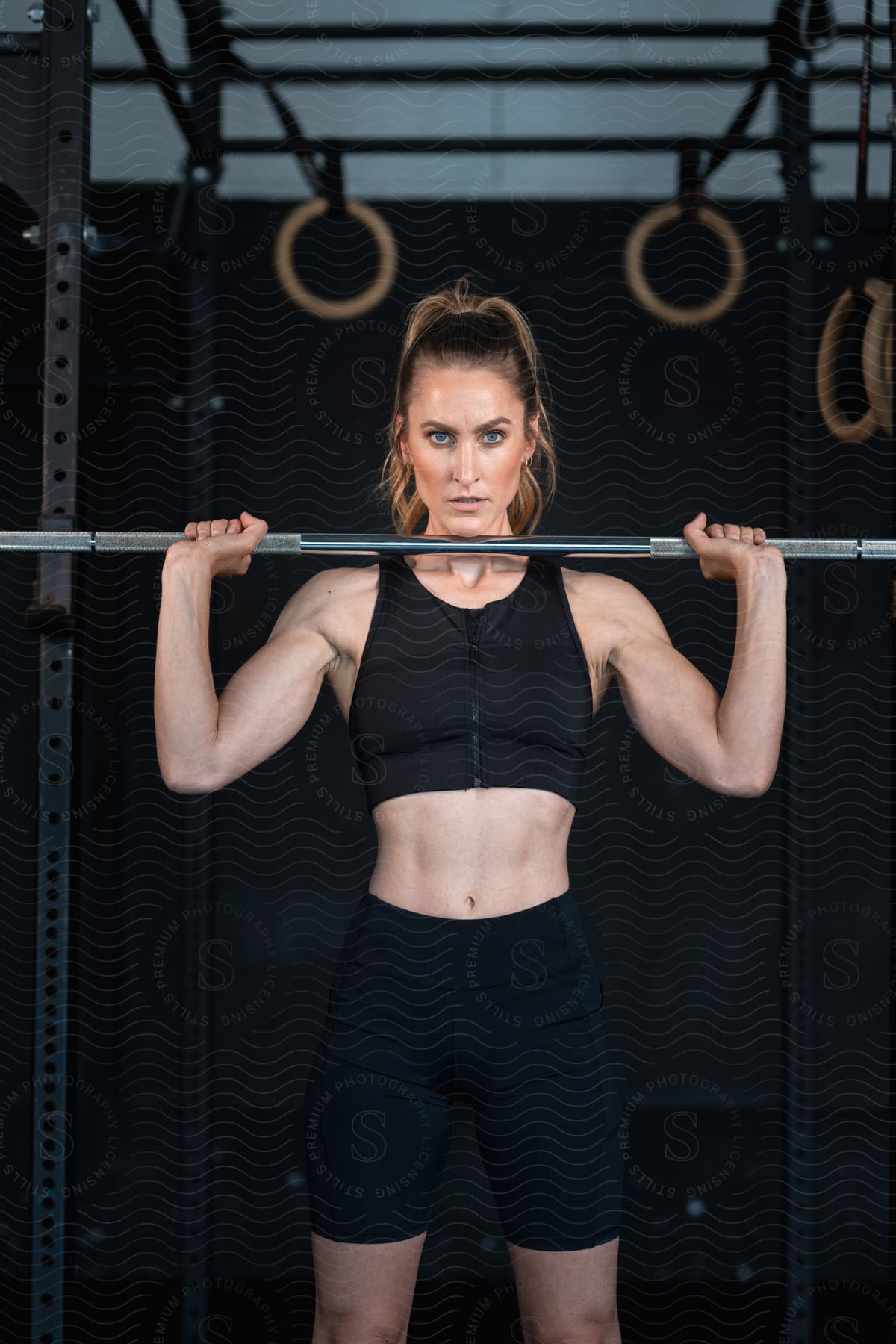 A woman holds a weight lifting bar at shoulder level while modeling fitness apparel.
