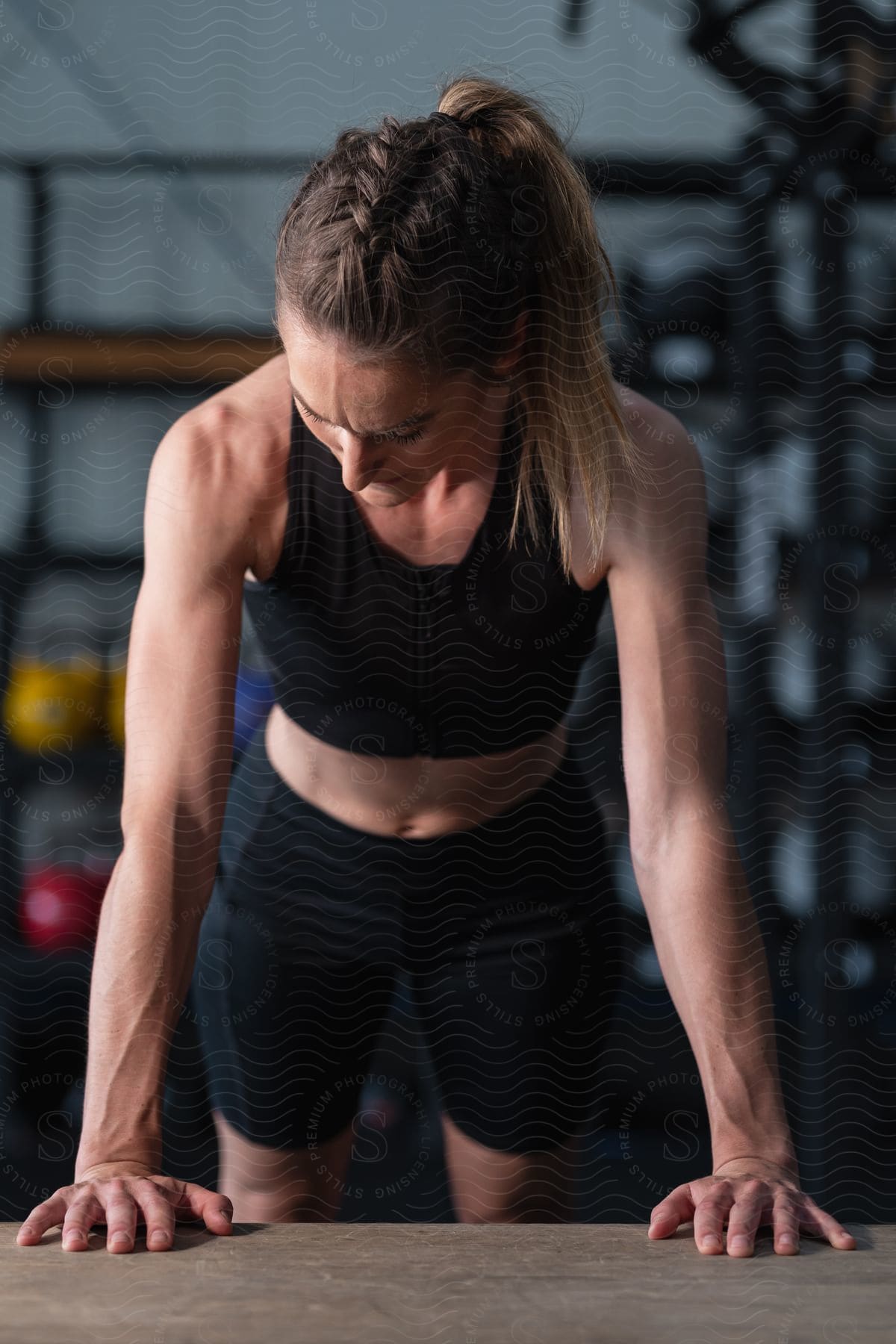 a muscular blond hair woman in a black top and shorts doing a push up on a table in a gym