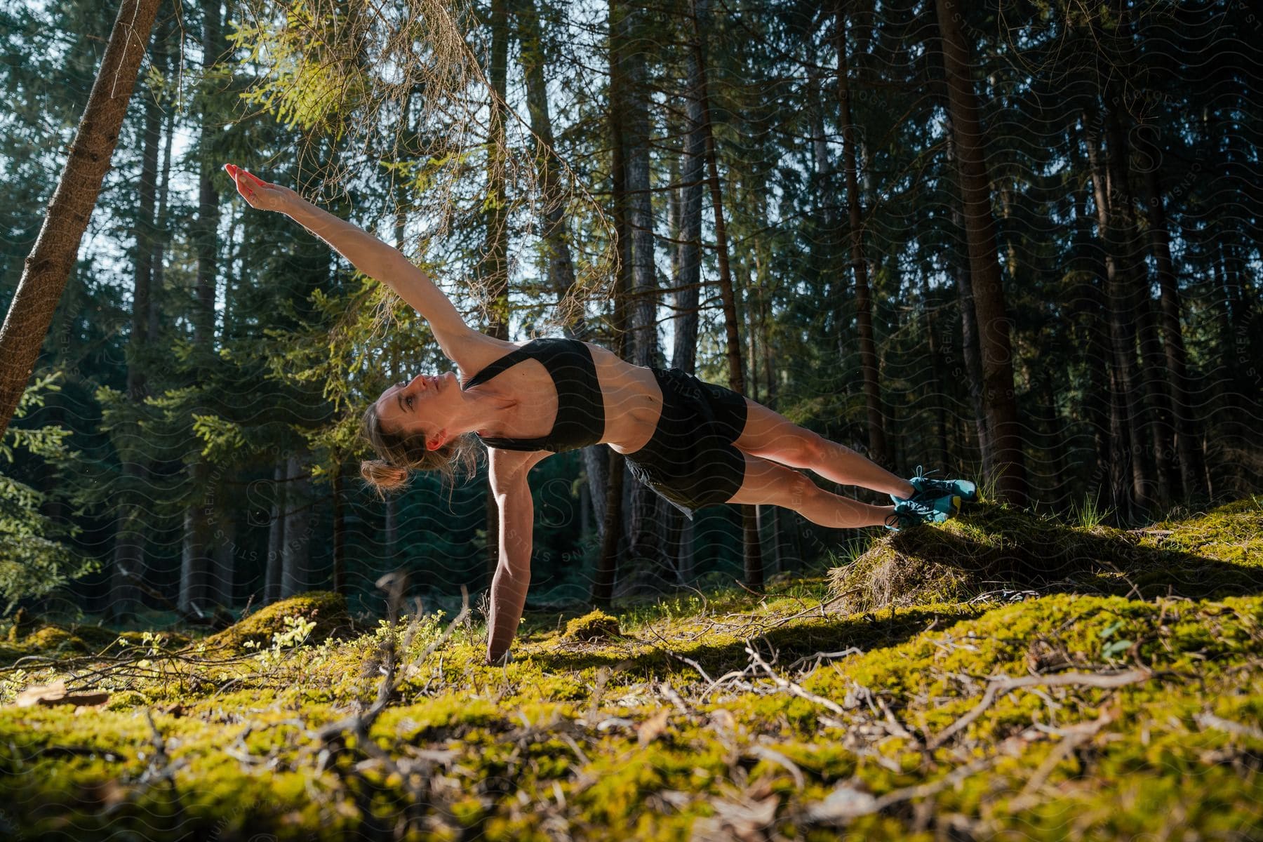 Woman wearing a black top and shorts stretches in the forest