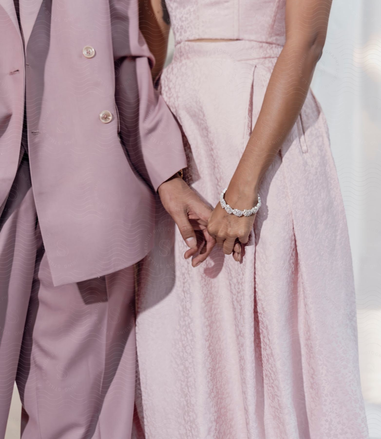 A woman in a pink dress holds onto the fingers of a man in a pink suit, creating a sweet and harmonious connection.