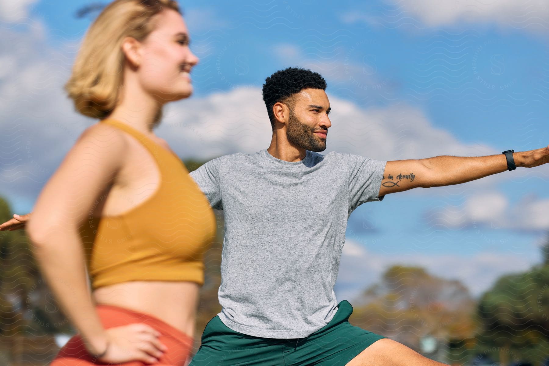 Man stretching his arms, and the woman beside him with hands on her waist, both in fitness attire.