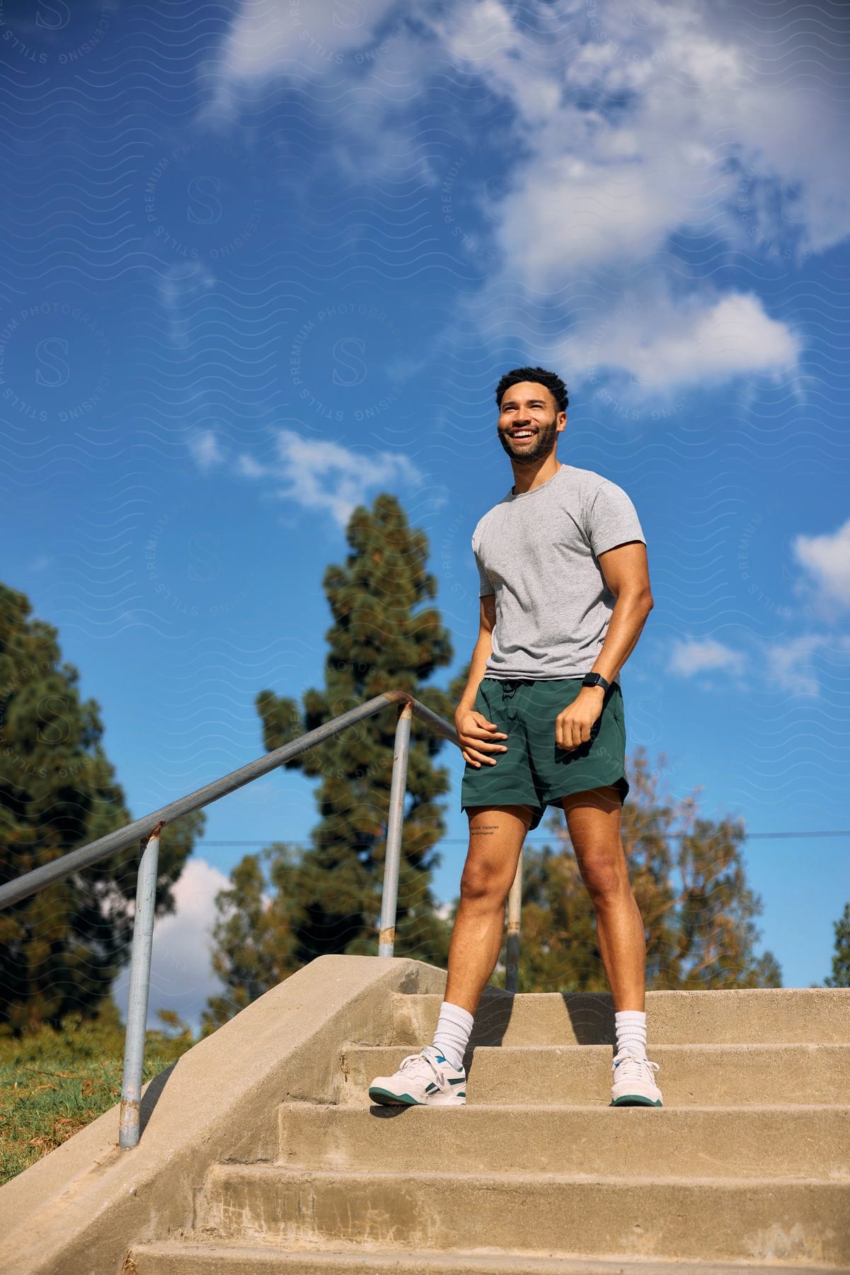 a man ith beared wearing shorts and a shirt standing next to a handrail on a staircase laughing