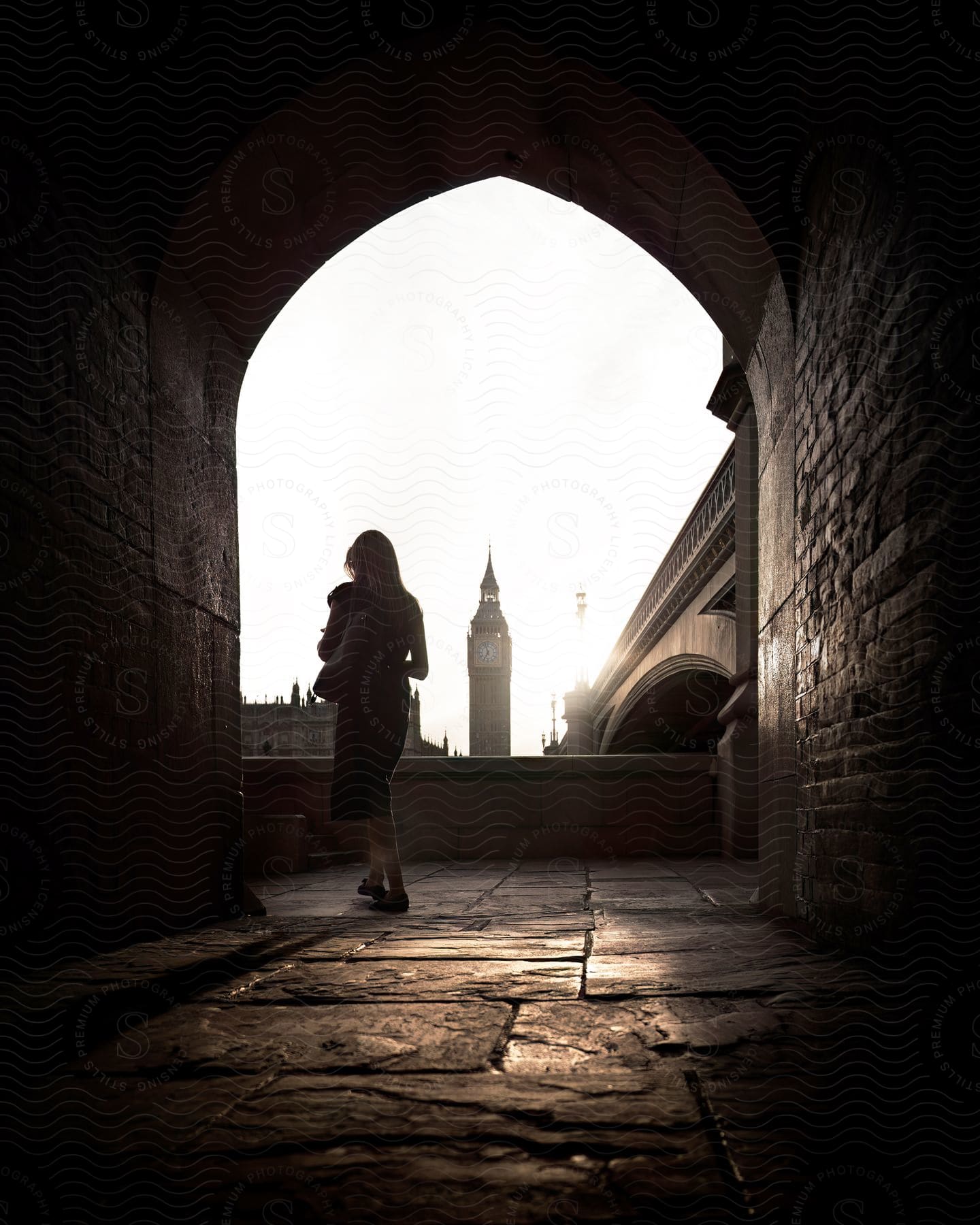 A woman exits a concrete tunnel across from Big Ben and Westminster Abbey.