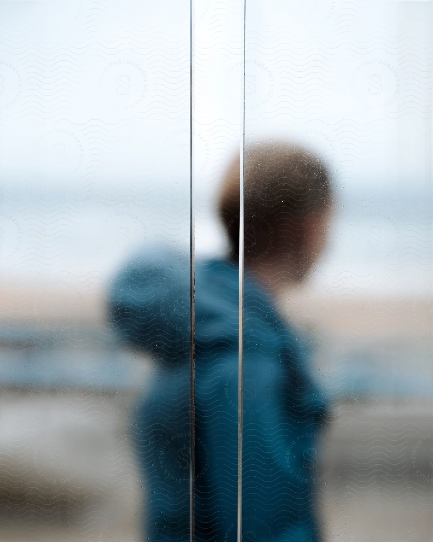 View through a steamed window of a young man standing outside wearing a hooded jacket on the beach