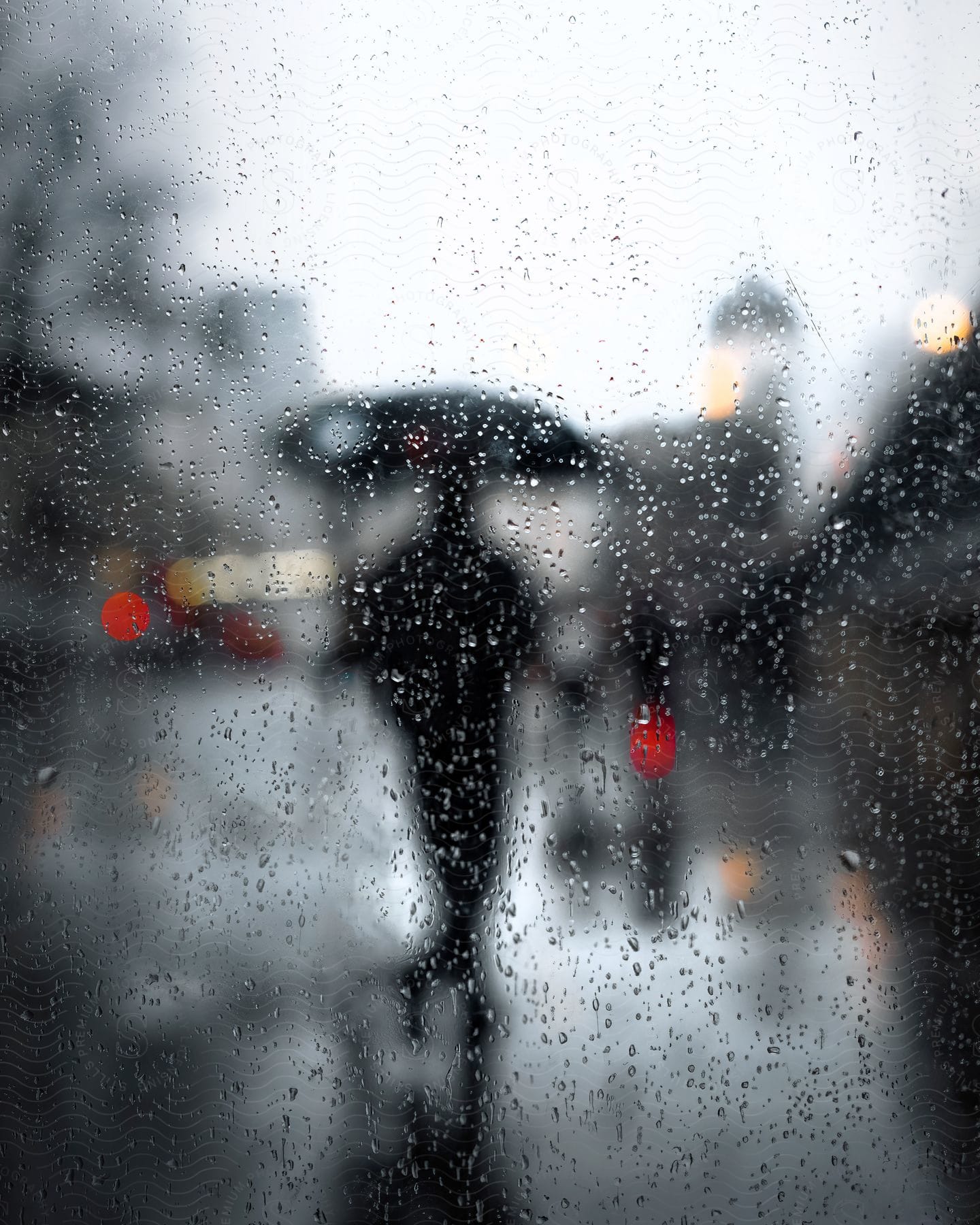 A man with an umbrella walking on the road, seen through a car window with water droplets.