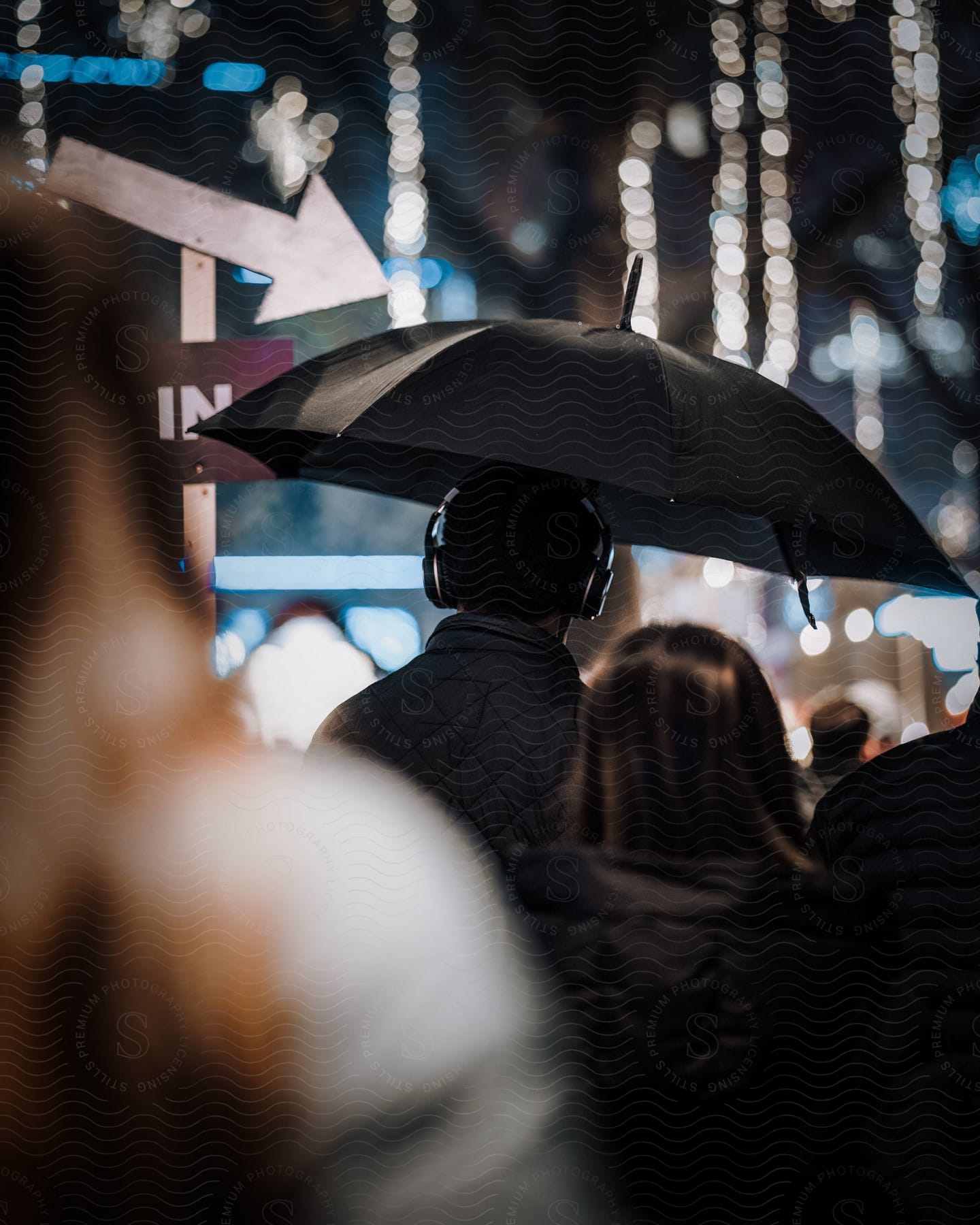 A man in headphones walking down the street with an umbrella.