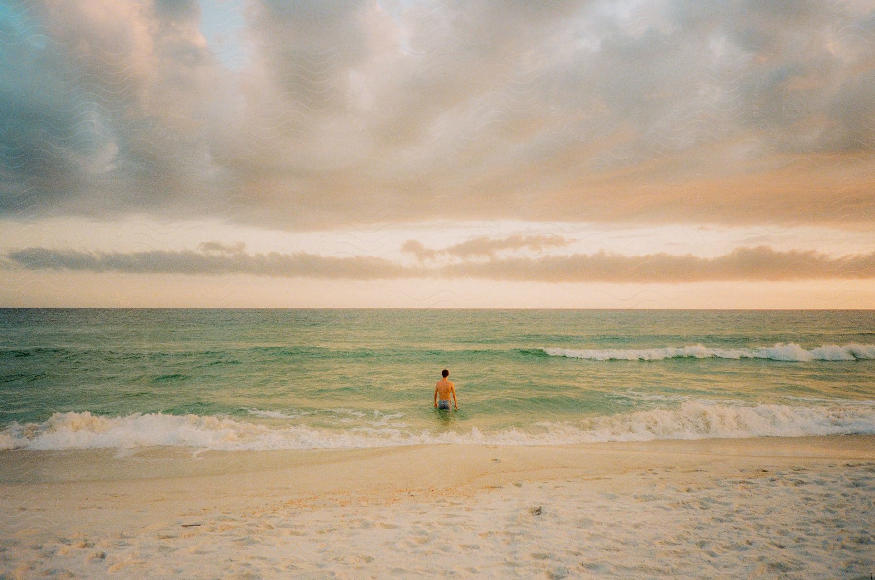 A man walks into the water at the beach as waves roll into shore