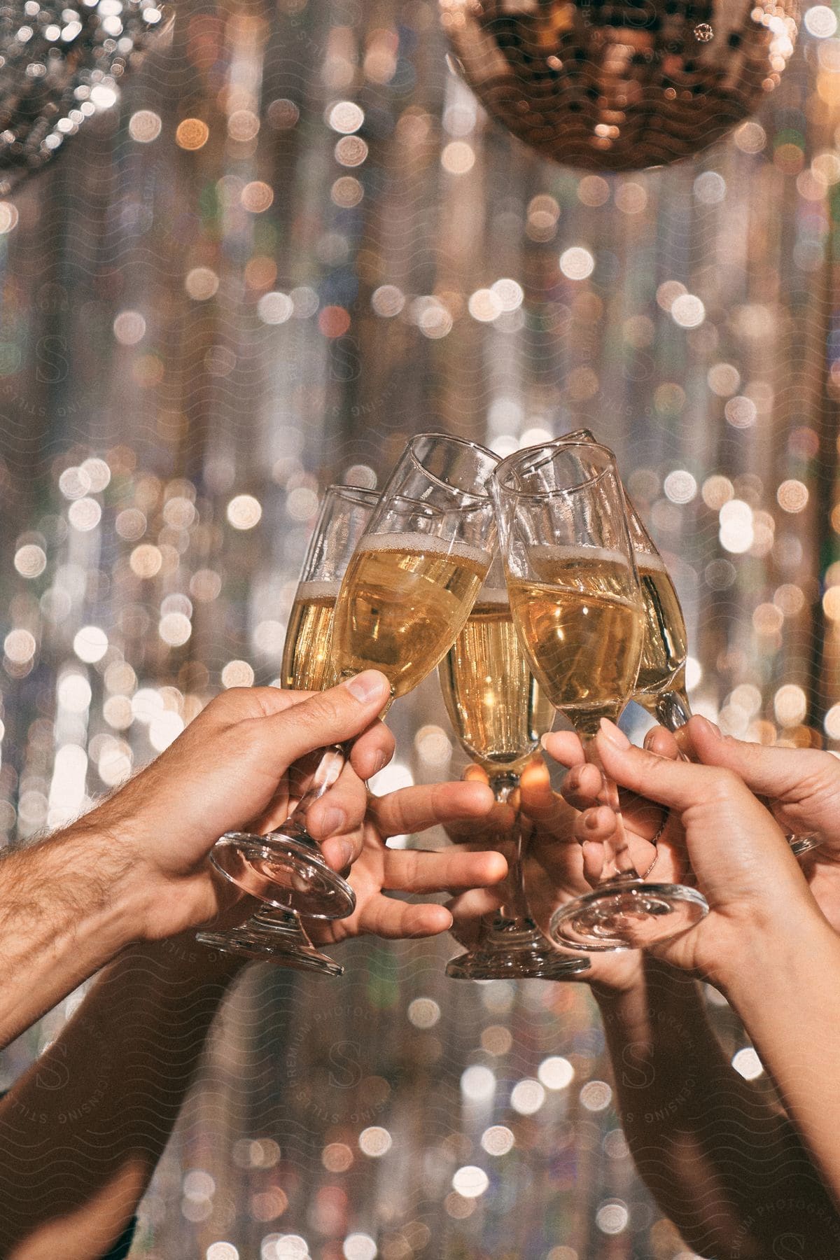 Hands of people toasting with champagne glasses against a background with a disco ball.