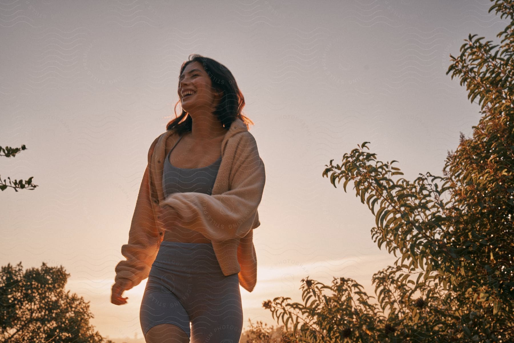 A woman laughing while running in nature at sunset.