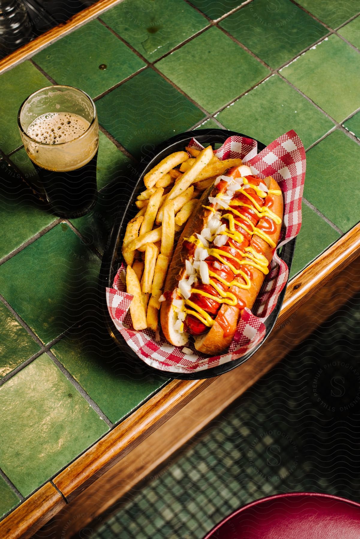 Hotdog and fries in a basket next to a glass of pop on a counter