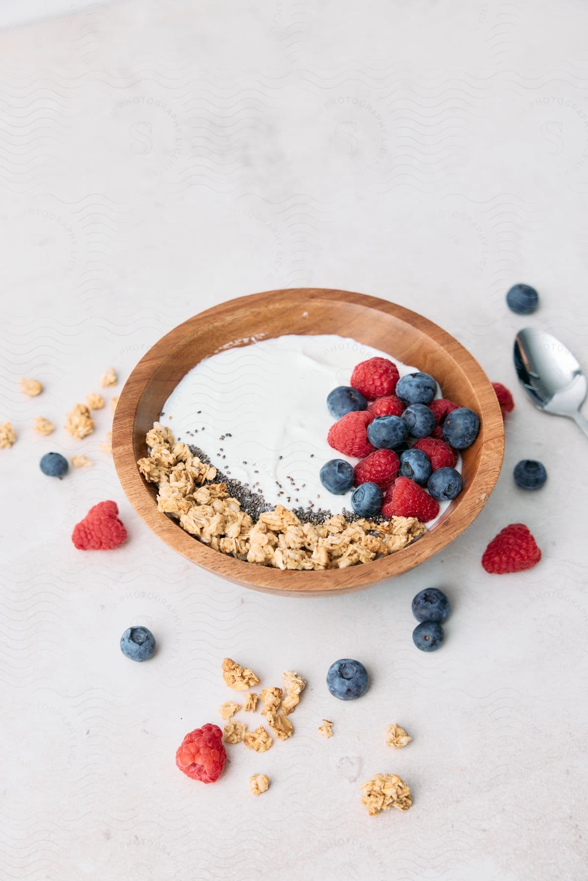 Milk in a bowl with cereal and blueberries and raspberries and scattered on the table with a spoon