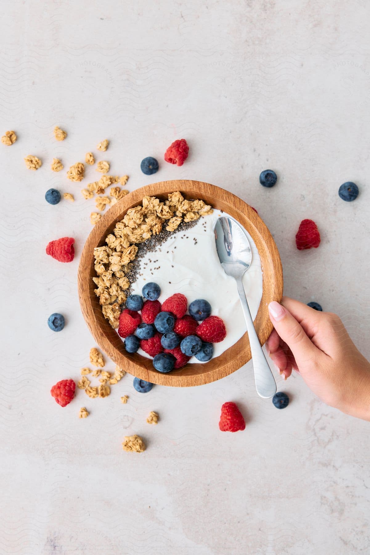 A woman's hand touches a bowl of granola, yogurt and fresh berries.
