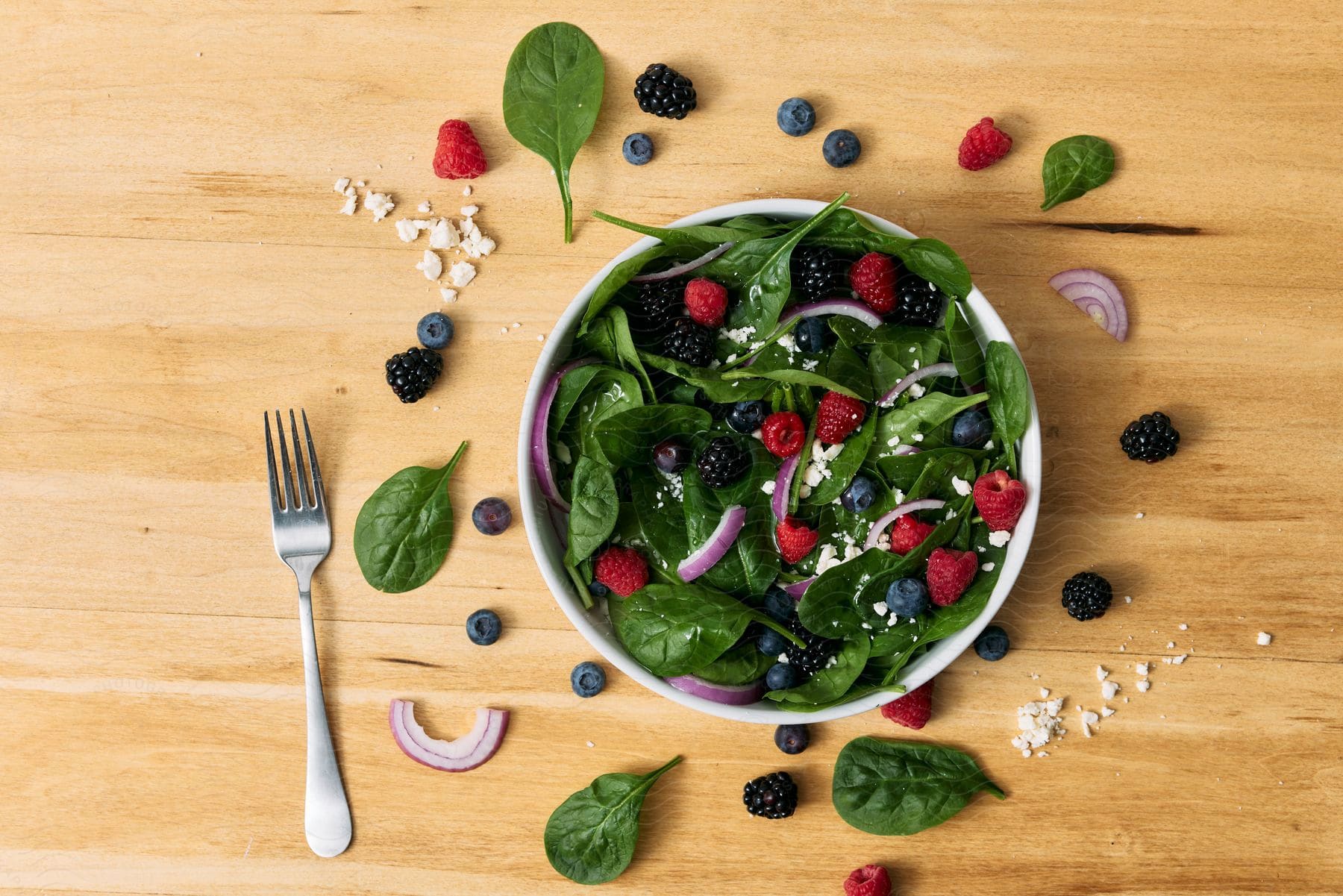 A bowl with a salad of spinach, berries and feta cheese.