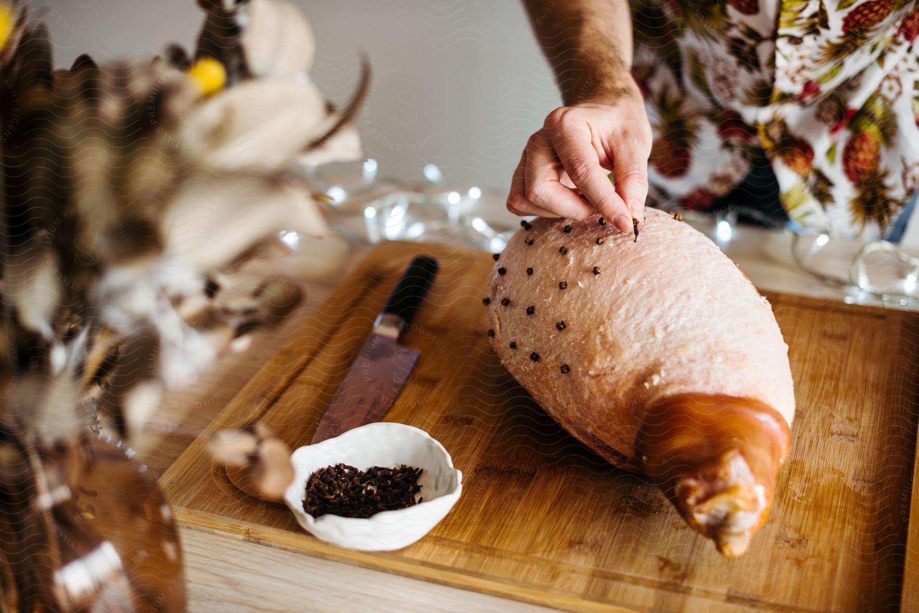 A man stands over an uncooked ham on a cutting board as he covers it with cloves.