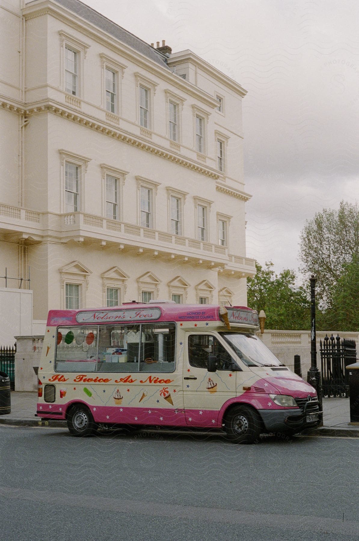 A pink and white ice-cream truck parked in front of an office building on a cloudy day.