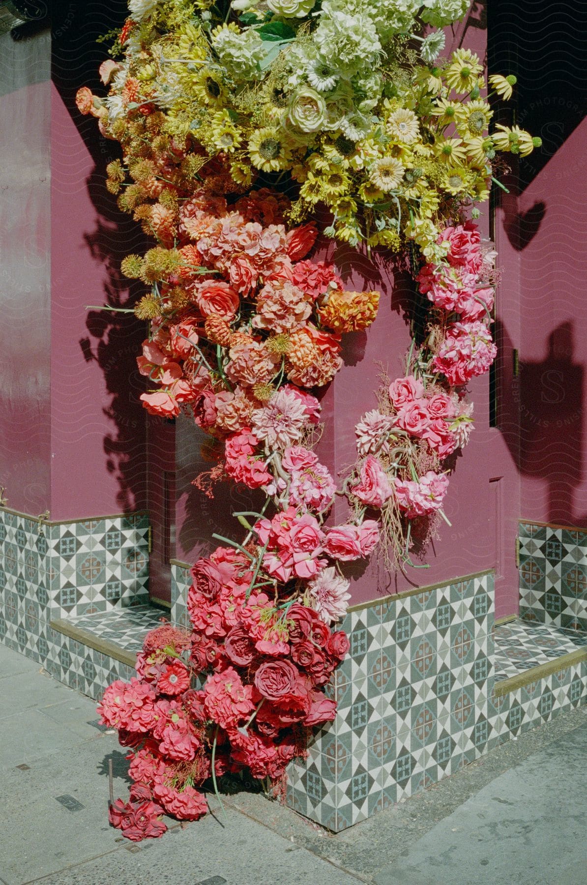 A colorful wreath made of pink and yellow flowers hangs on a corner wall at the entrance of a purple house.