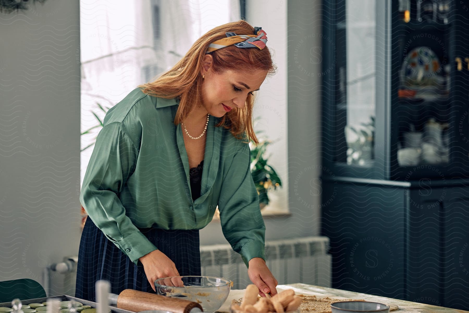 A woman is standing over her kitchen table getting her ingredients and bowls ready with her rolling pin and biscuits on the table