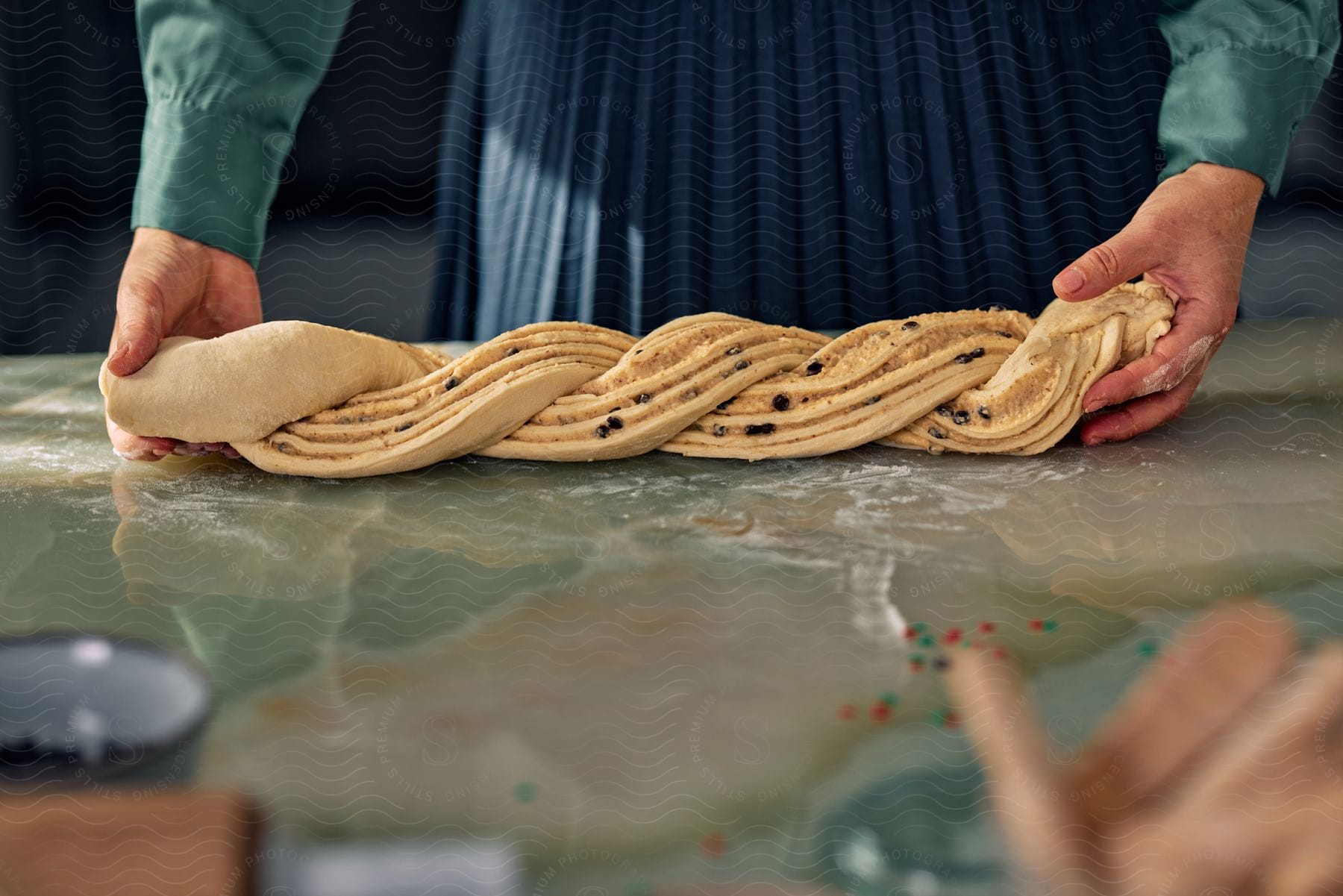 A person stands at a counter from the waist down shaping and twisting raw dough.