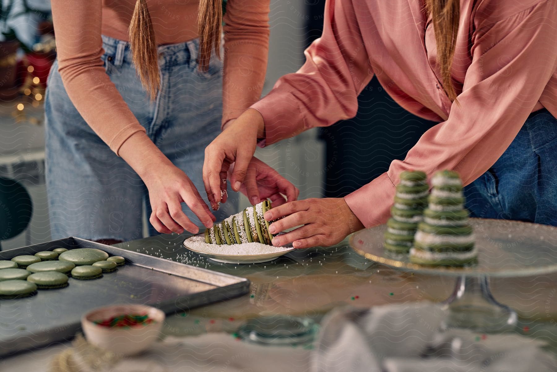 Two sisters are making a Christmas tree from green macaroons.