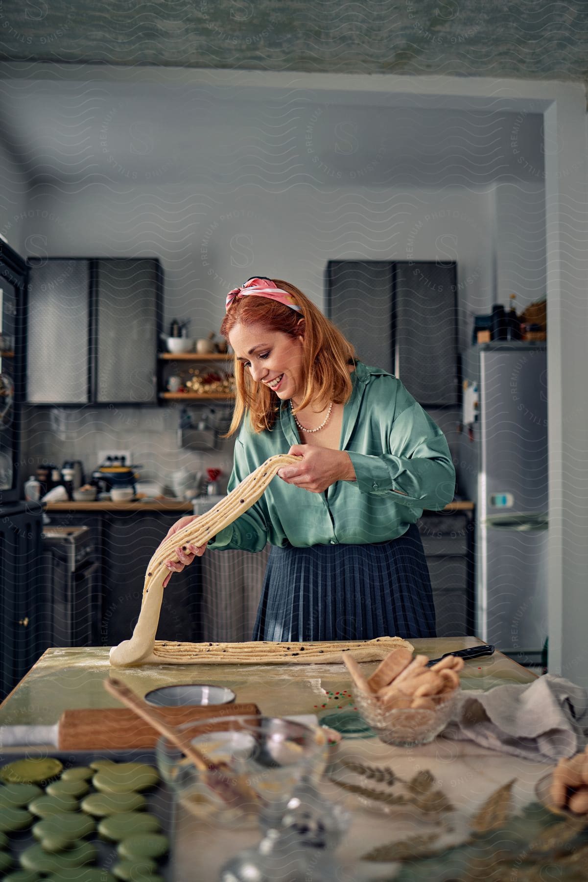 Stock photo of a woman is standing in her kitchen baking and smiles as she stretches the bread dough