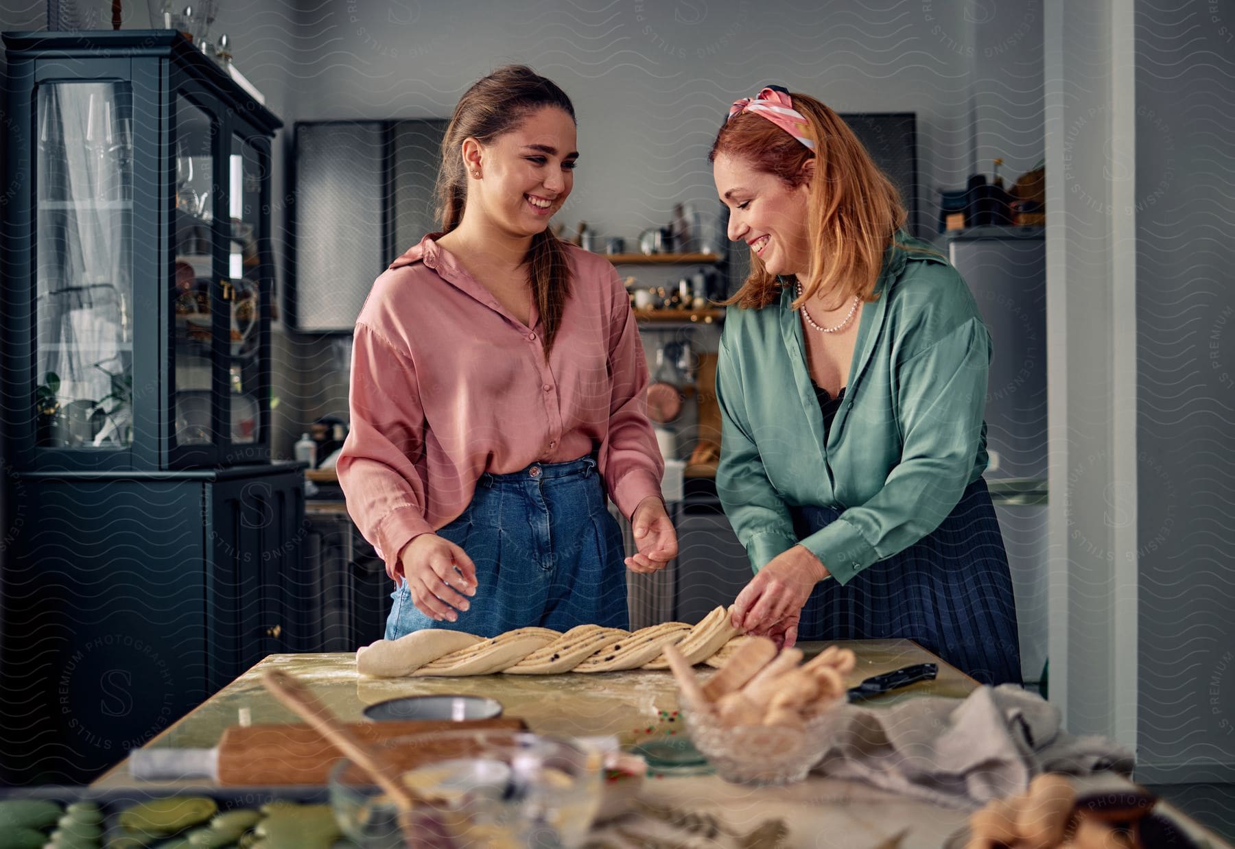 Mother and daughter are standing in the kitchen smiling and laughing as they work with bread dough