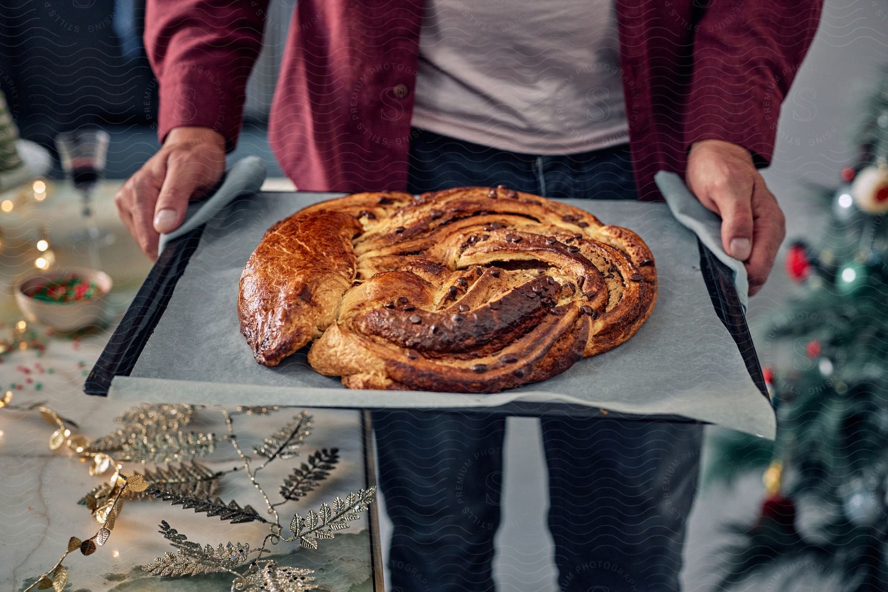 A man holding a pan with a Christmas pastry wreath.