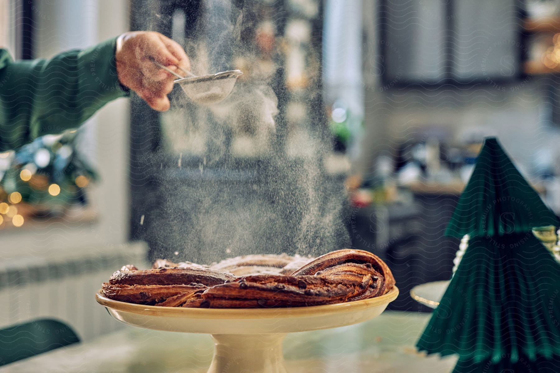 An adult is shaking powdered sugar on top of a ring of pastry bread.