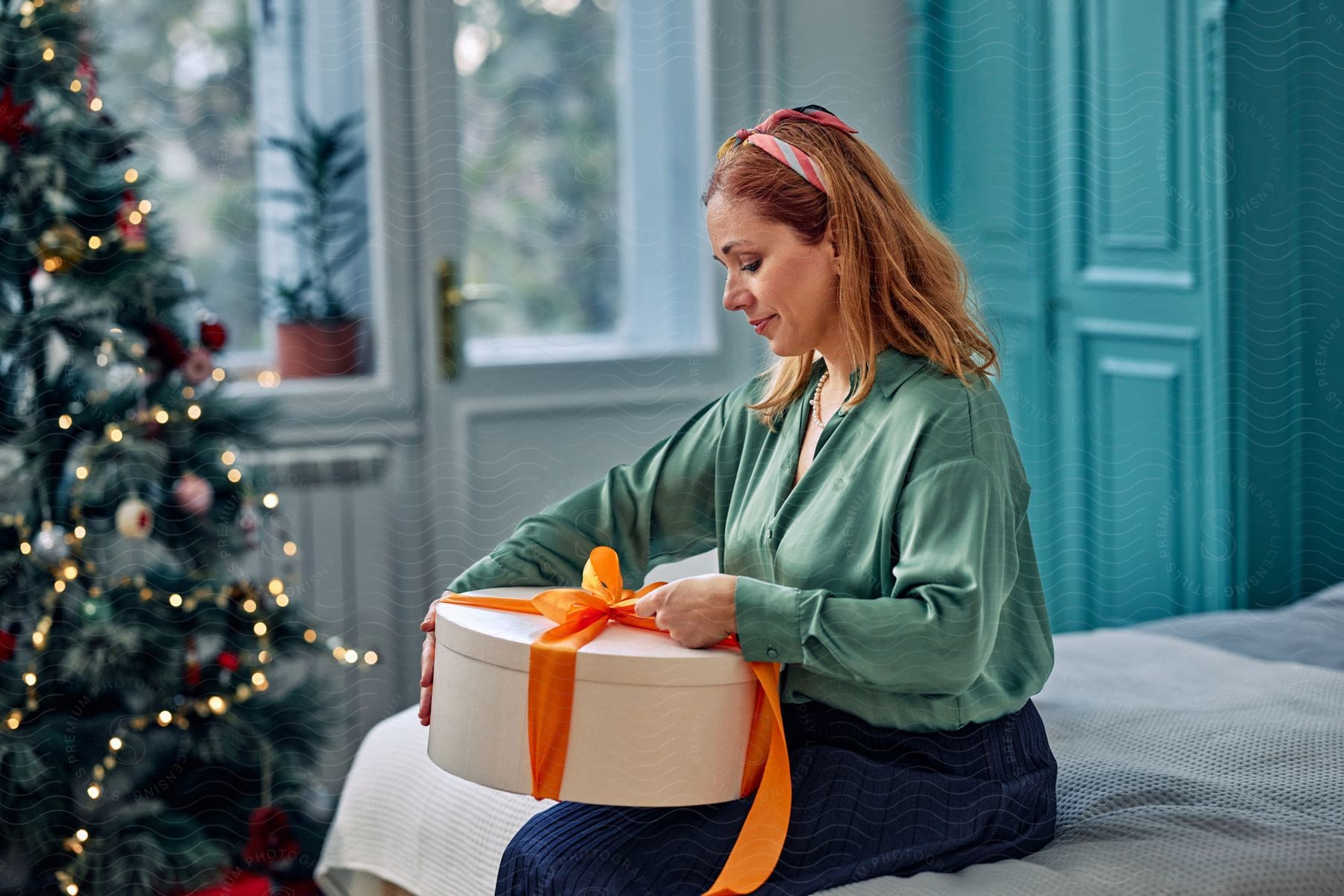 Woman sitting next to a christmas tree opening a present