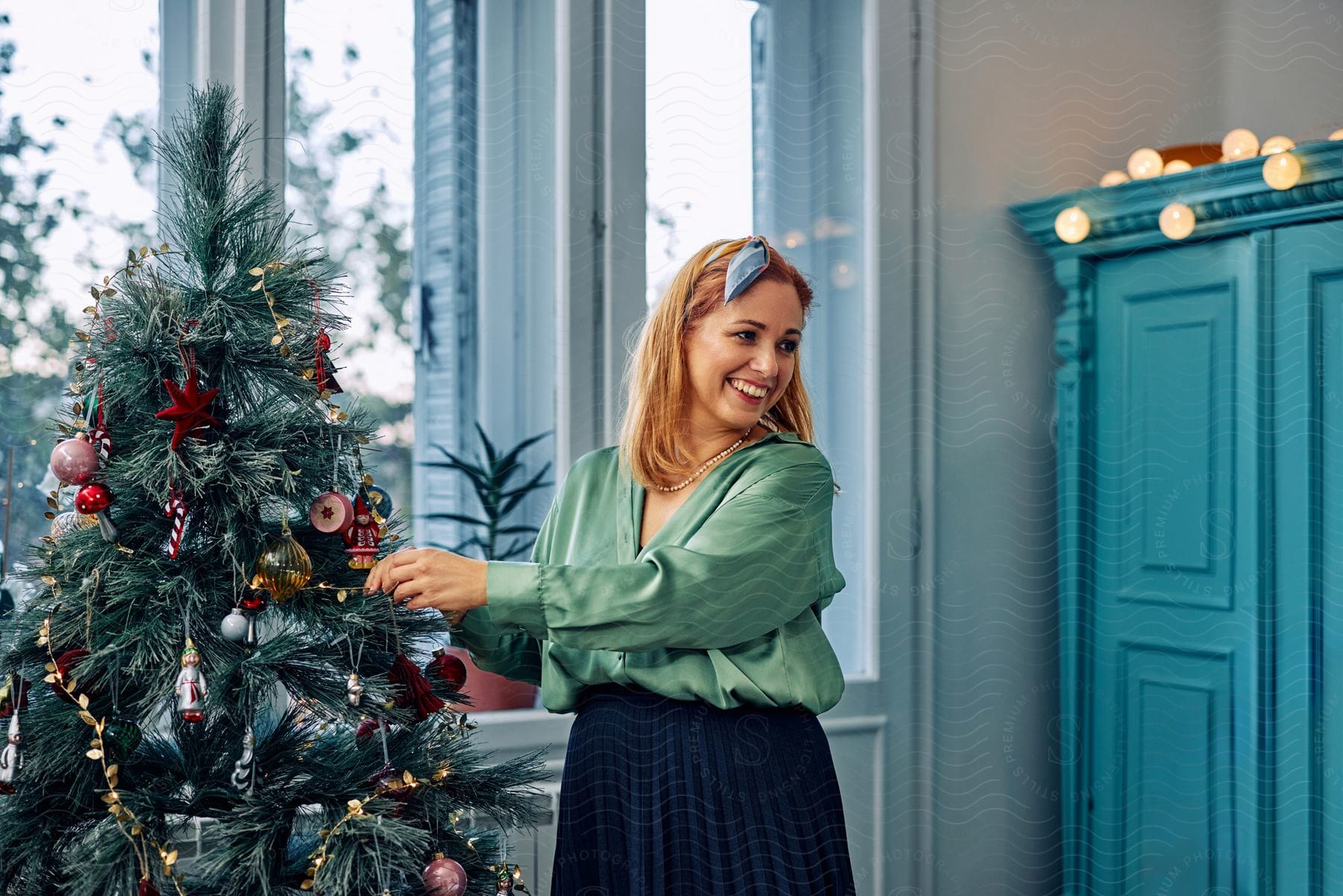 A woman smiles as she puts an ornament on a decorated Christmas tree.