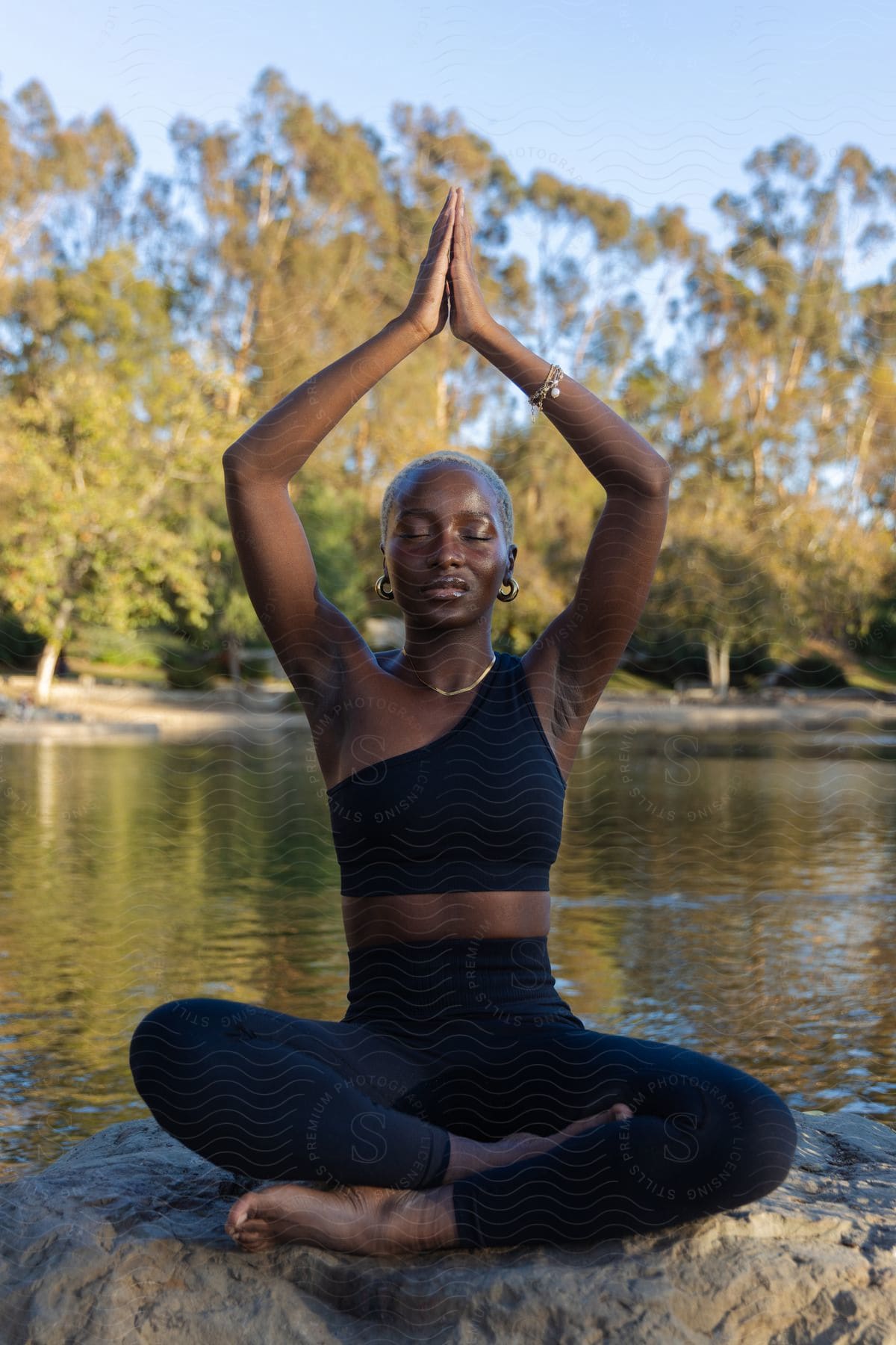 An African woman is sitting on a rock on the riverbank in lotus yoga pose.