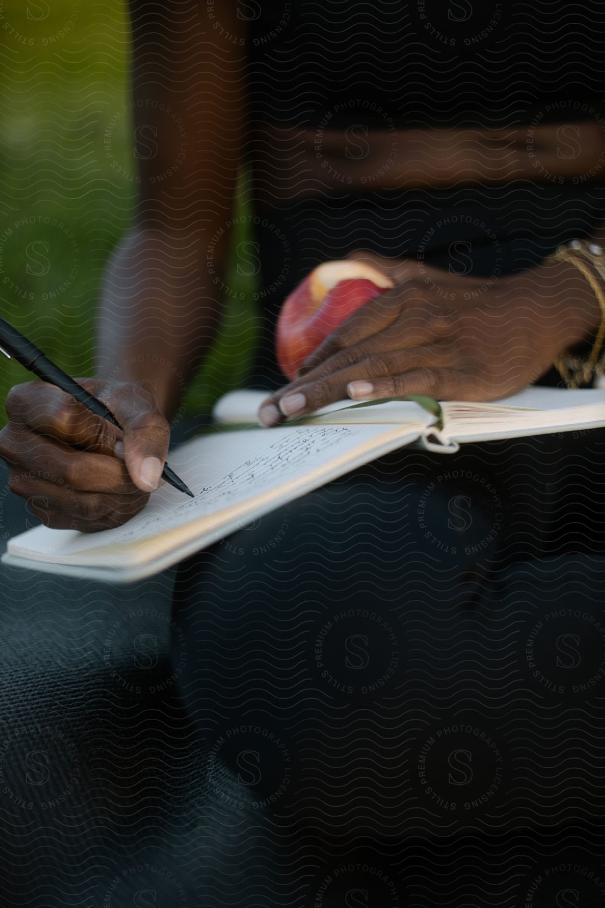 A woman writing in a journal while eating an apple in the park.