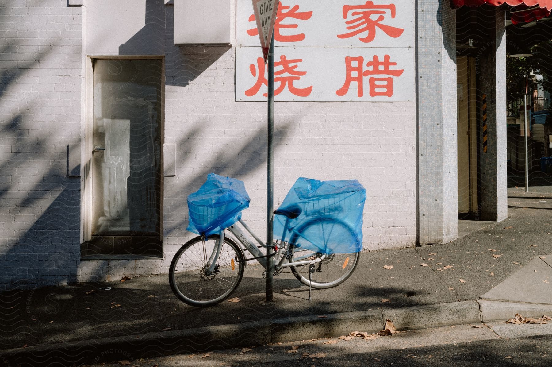 A bicycle covered in blue plastic bags parked on a sidewalk.