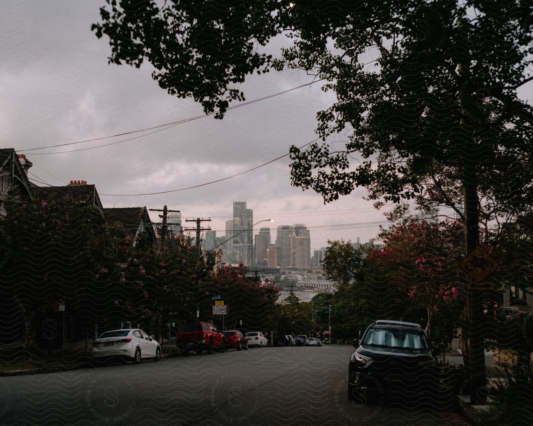 a city street with cars parked on the side of it and a cloudy sky in the background with buildings in the distance