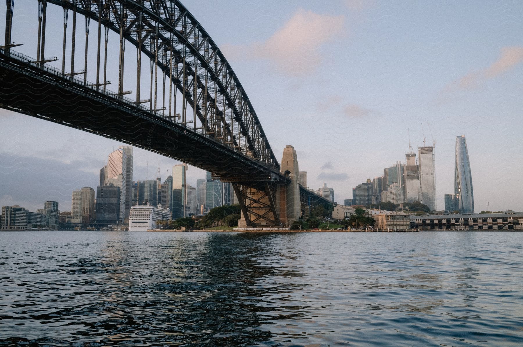 A suspension bridge arcs over water into a large city downtown.