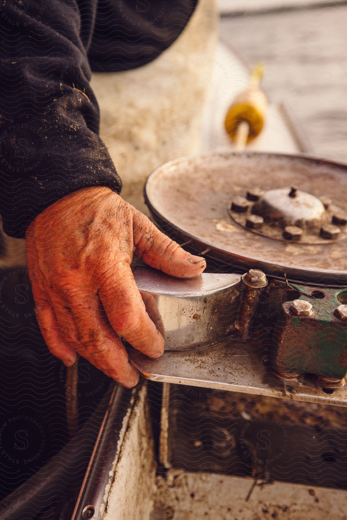 Close-up of a weathered hand operating machinery, with signs of manual labor and machinery parts in view.