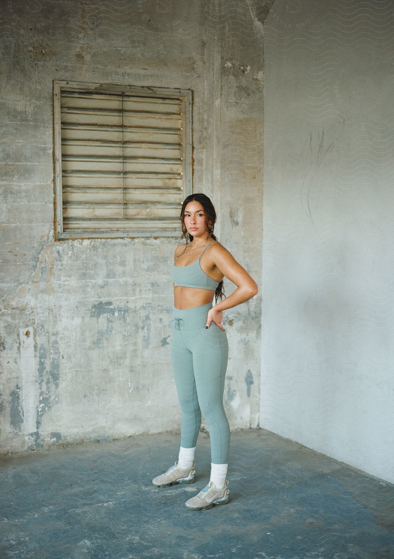 A young woman with dark hair stands while modeling fitness apparel and tennis shoes.