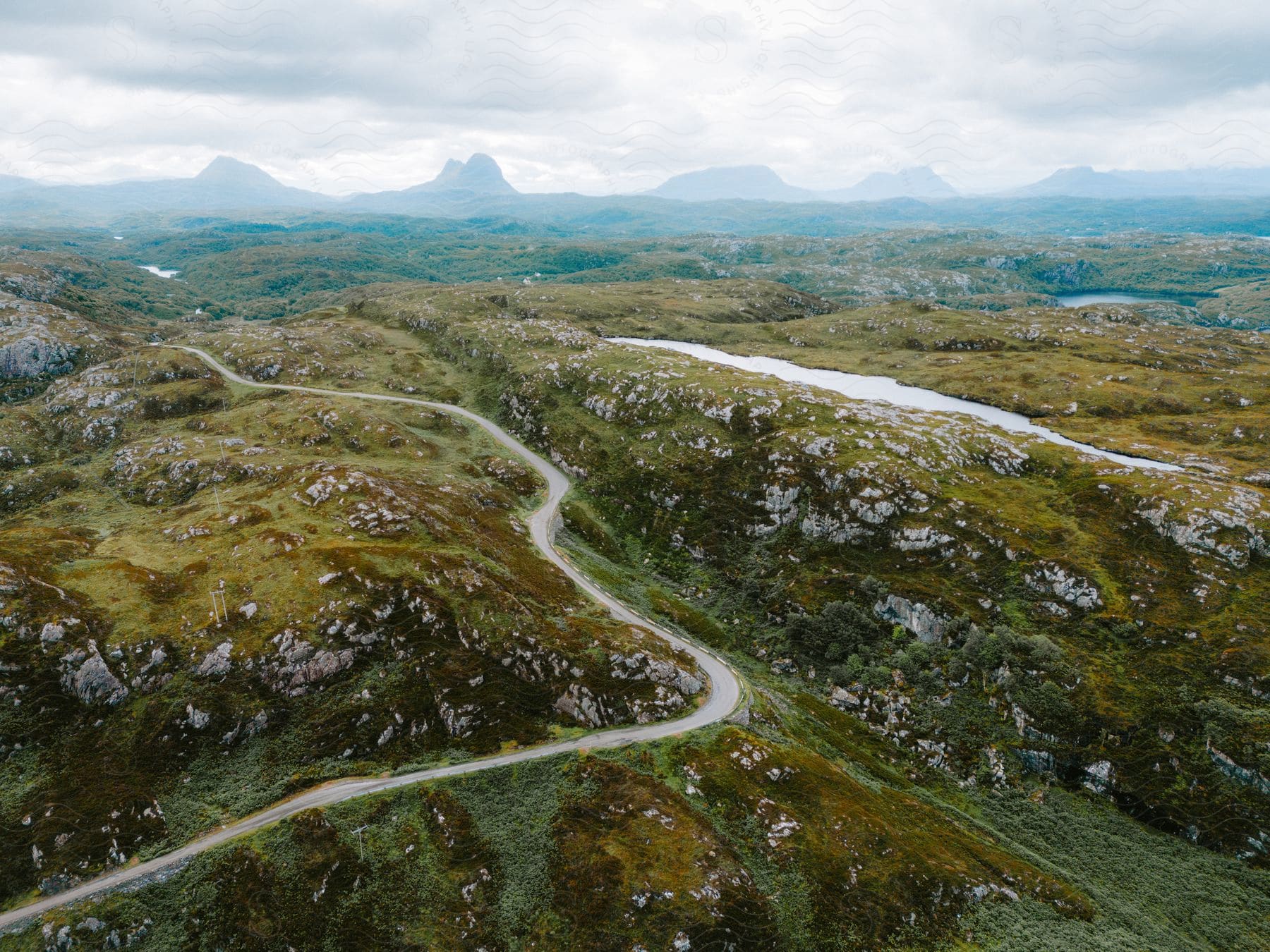 A winding road runs through highlands with mountains in the distance.