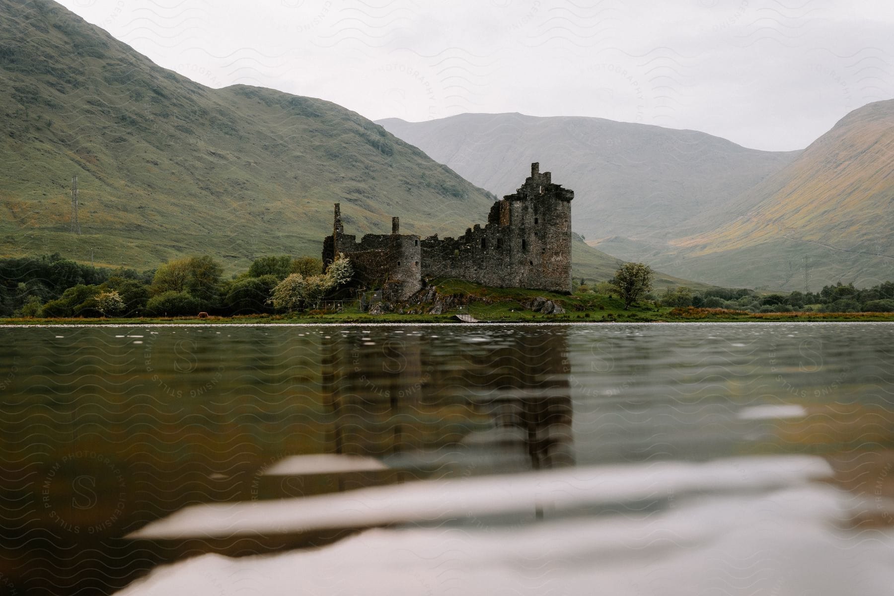 An old castle stands along the coast with mountains in the distance