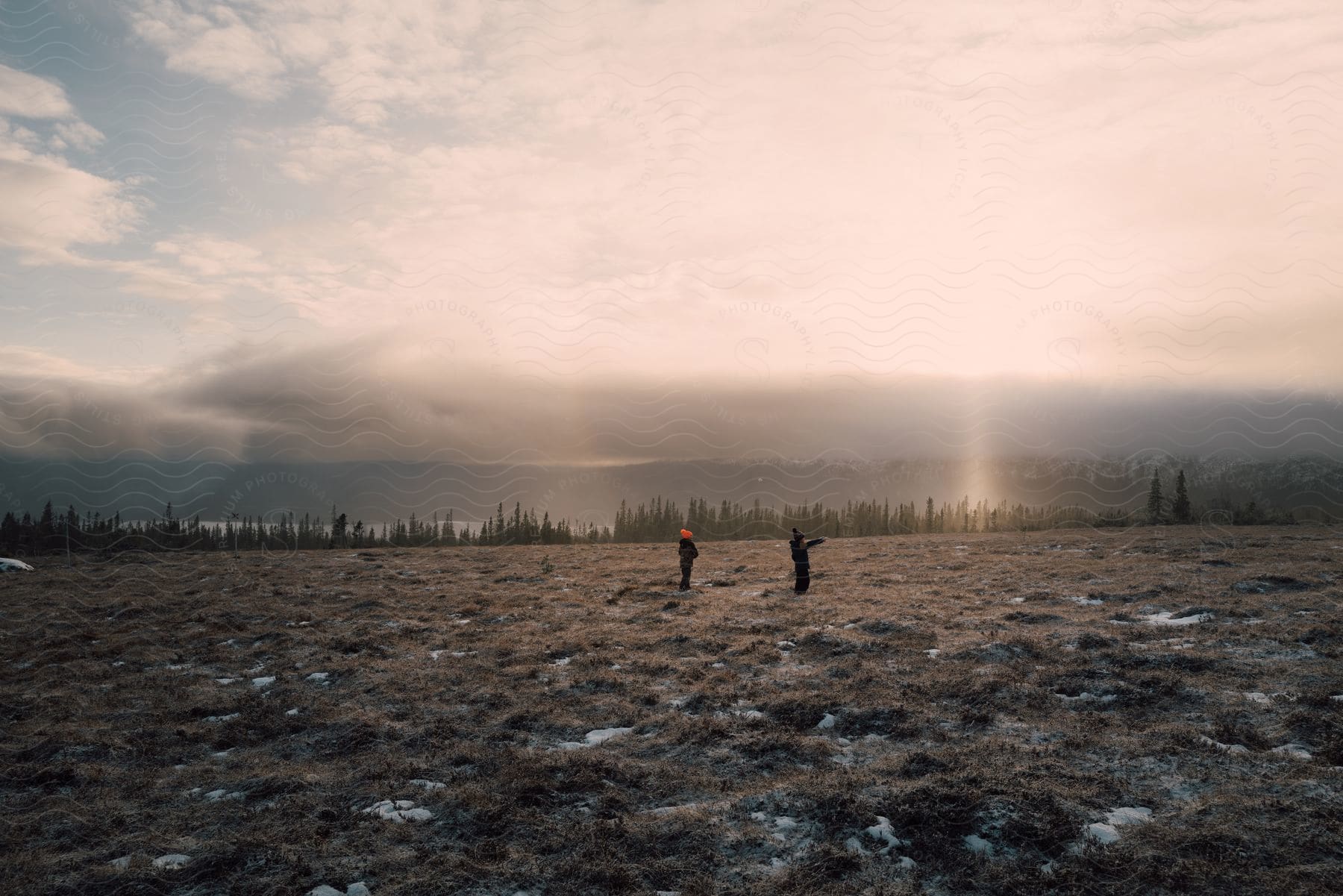 Two boys stand in the terrain, bathed in sunlight, as the distant lake and forest come into view.