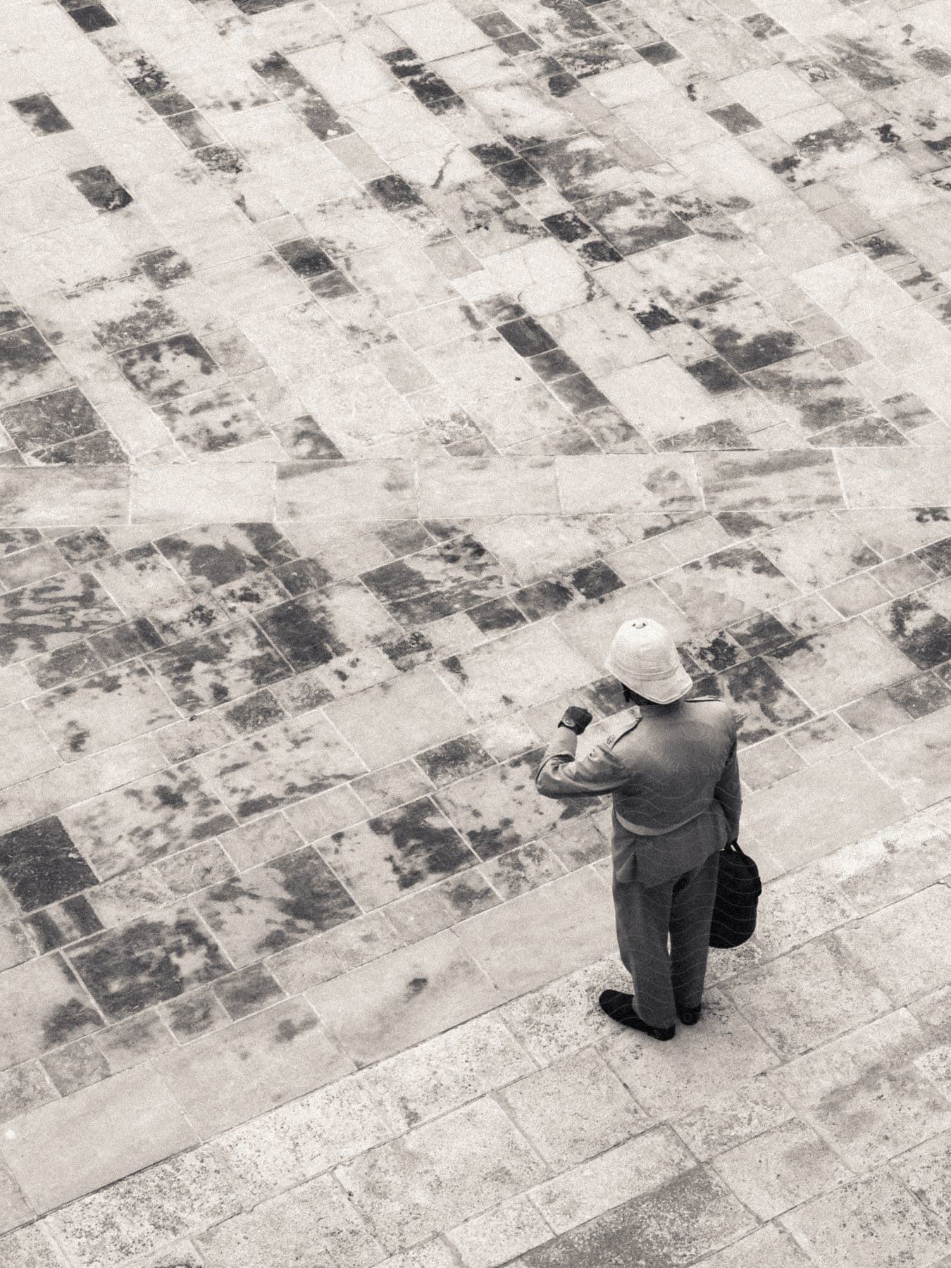 A man stands on the side of the street holding a bag and looking at his watch