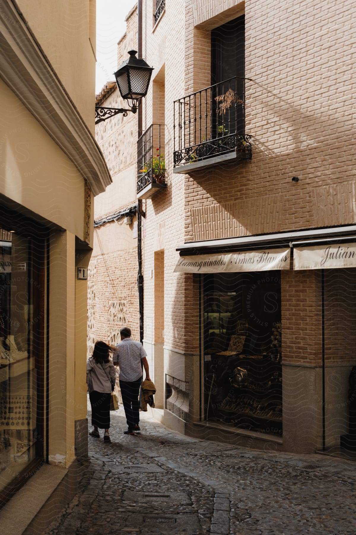 A man and a woman walk down a narrow street, passing by stores