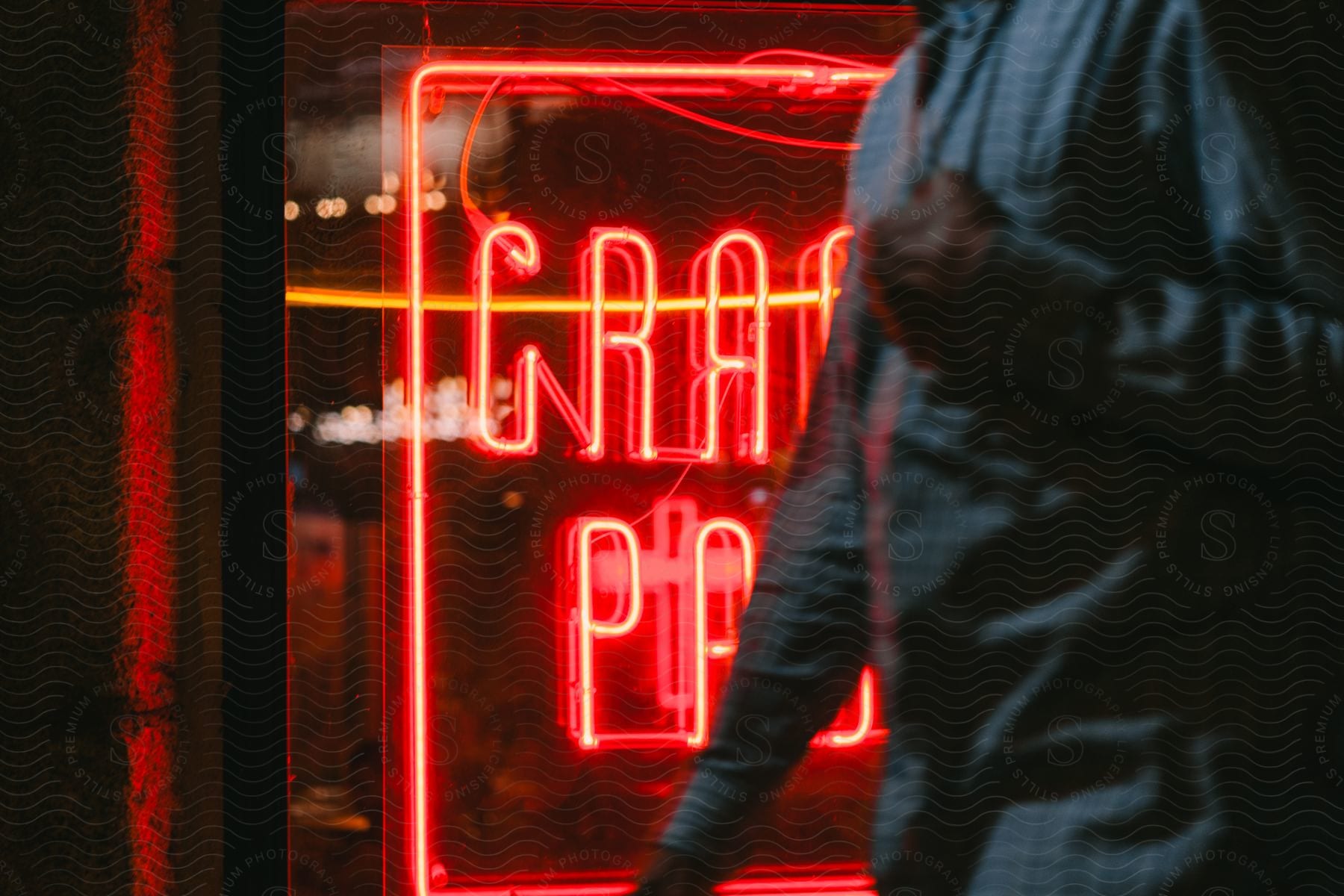 Man passing by a red neon panel in a glass window at night.