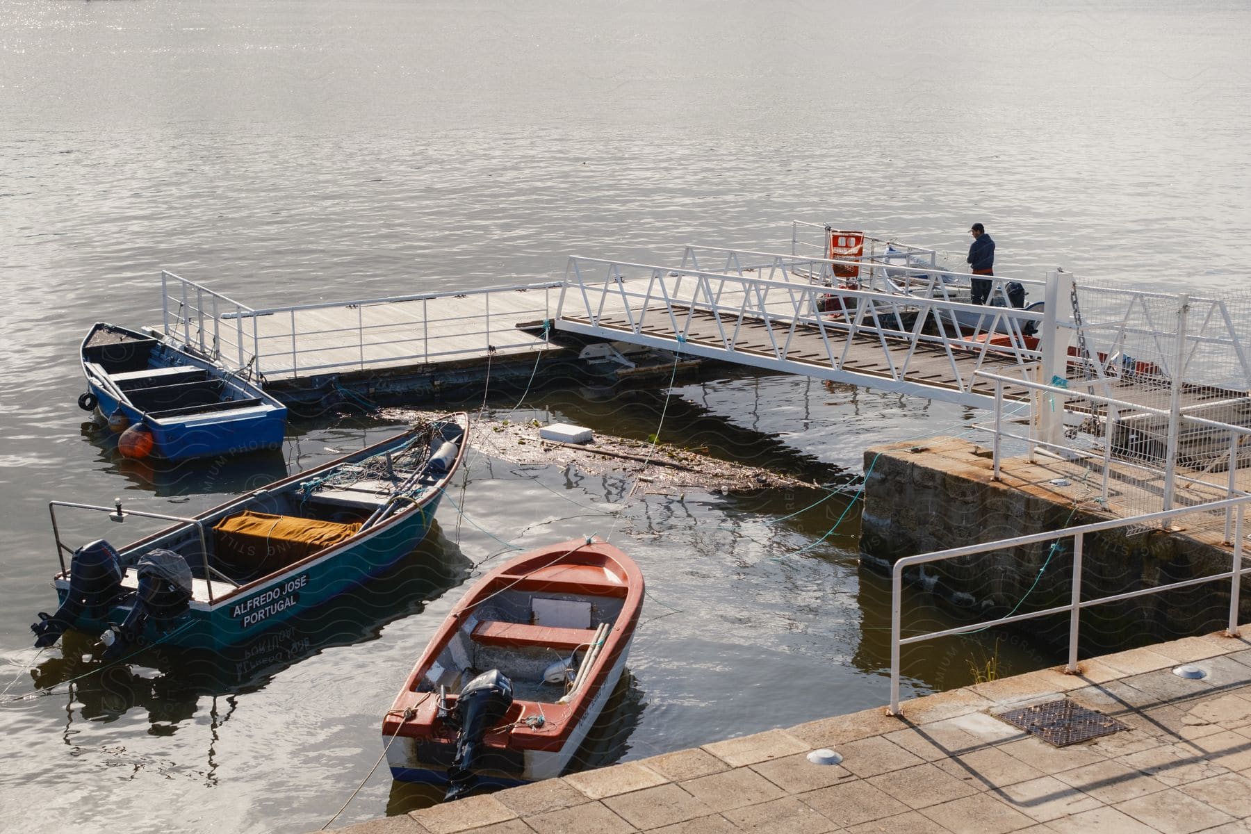 A man standing near some boats on a pier in the ocean.