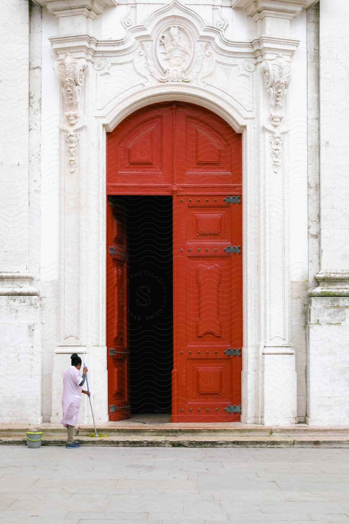 A woman mopping in front of a large door on an ancient building.