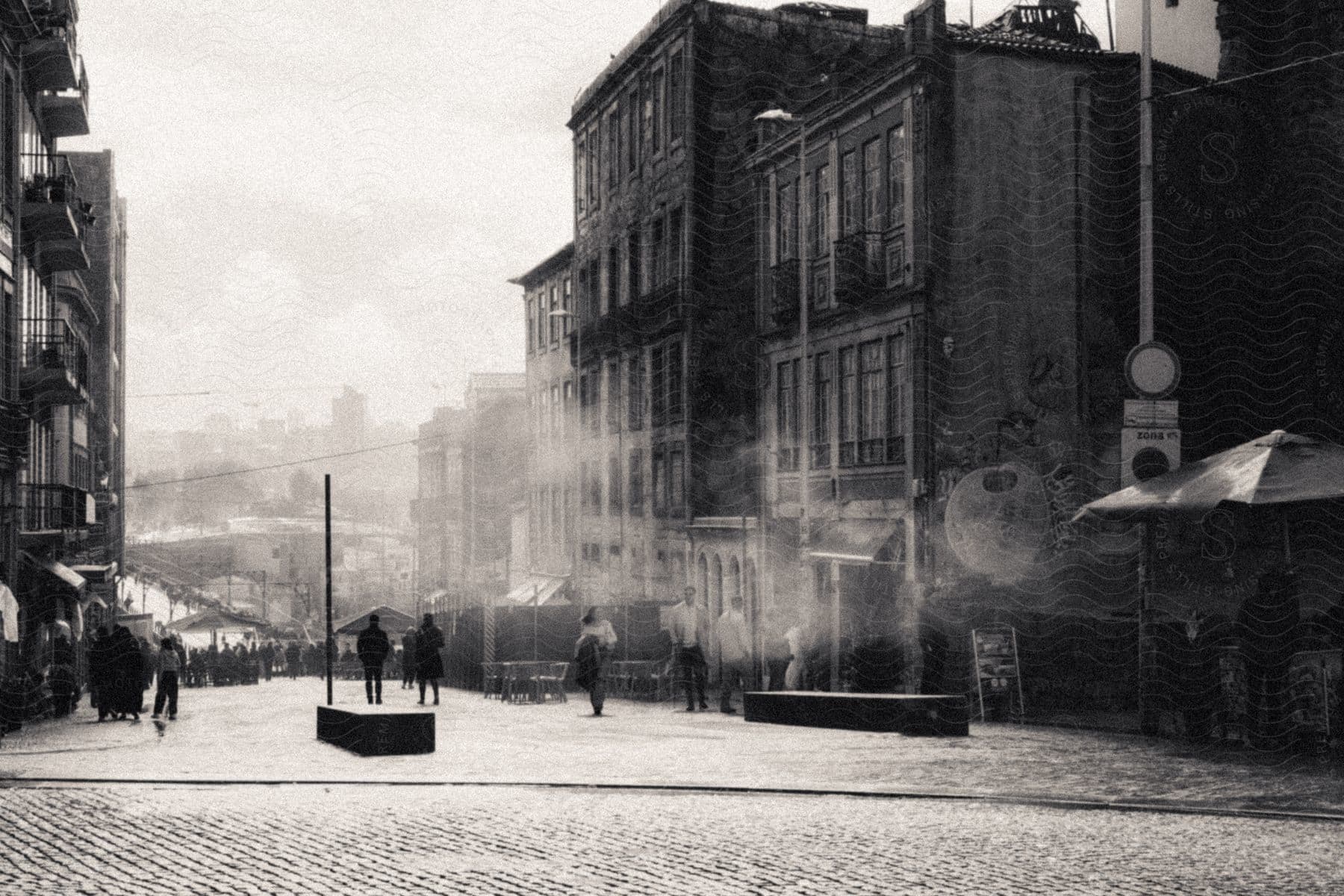 Black and white photo of people walking down a street amid old buildings.