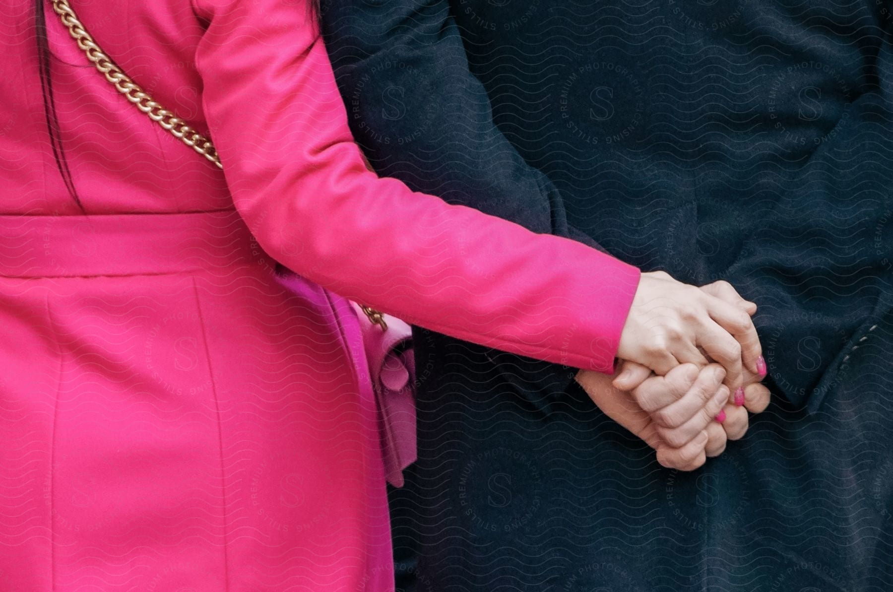 A woman in a black overcoat and another in a pink overcoat holding hands, expressing a connection amidst their distinct styles