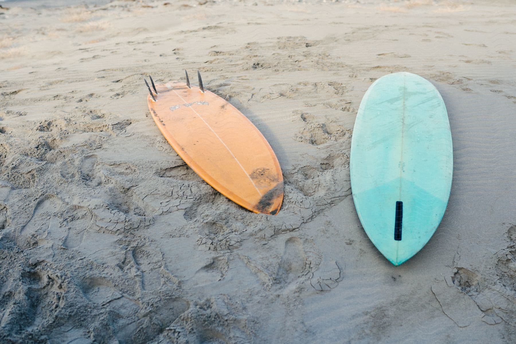 A blue and an orange surfboard on a beach.