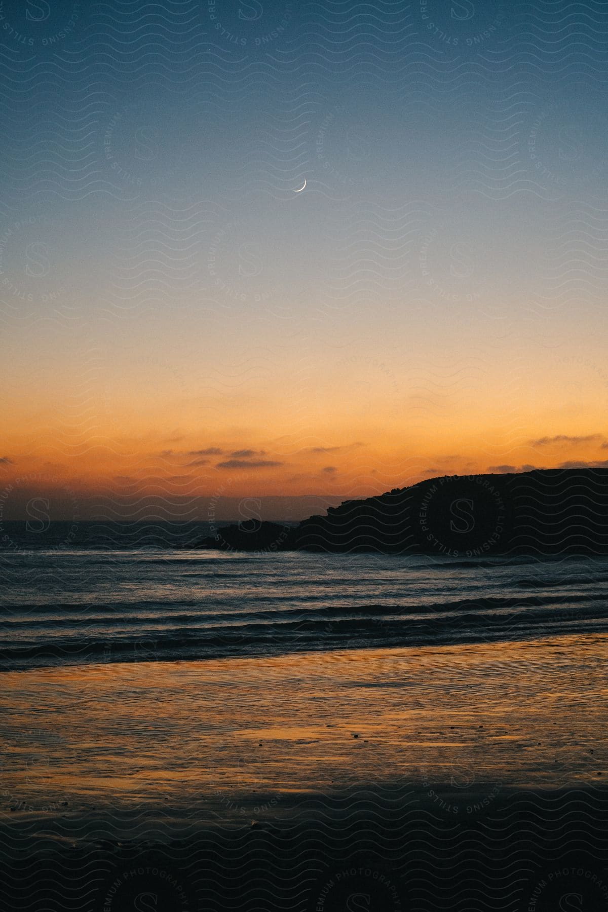 Panorama of a beach with calm waves and the orange sky at dawn.